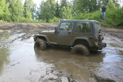 2003 Jeep TJ - A 2003 Jeep TJ is stuck deep in a muddy off-road trail, with trees and a person in the background.