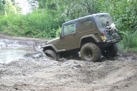 2003 Jeep TJ - A 2003 Jeep TJ navigates a muddy off-road trail, kicking up dirt and water.