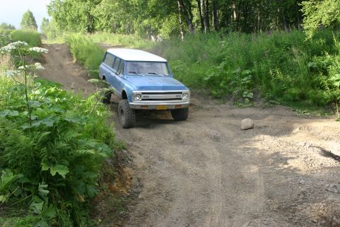 2003 Jeep TJ - A blue Chevrolet K5 Blazer navigates a dirt trail surrounded by lush green vegetation.