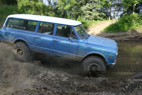 2003 Jeep TJ - A blue station wagon with a white roof navigates a muddy off-road course, with visible text on the rear window.