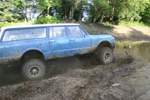 2003 Jeep TJ - Blue station wagon with white roof driving through mud, "56500" written on side window.
