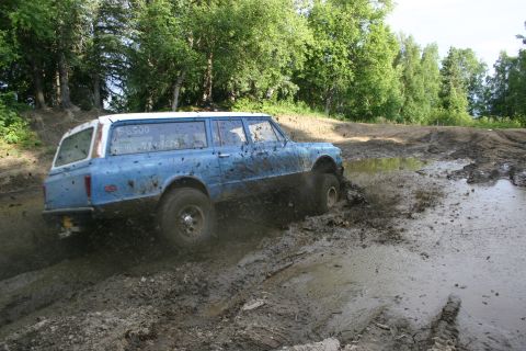 2003 Jeep TJ - A blue station wagon navigates a muddy off-road course, kicking up dirt and water.