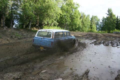 2003 Jeep TJ - Station wagon navigates a muddy off-road course, kicking up water and dirt.