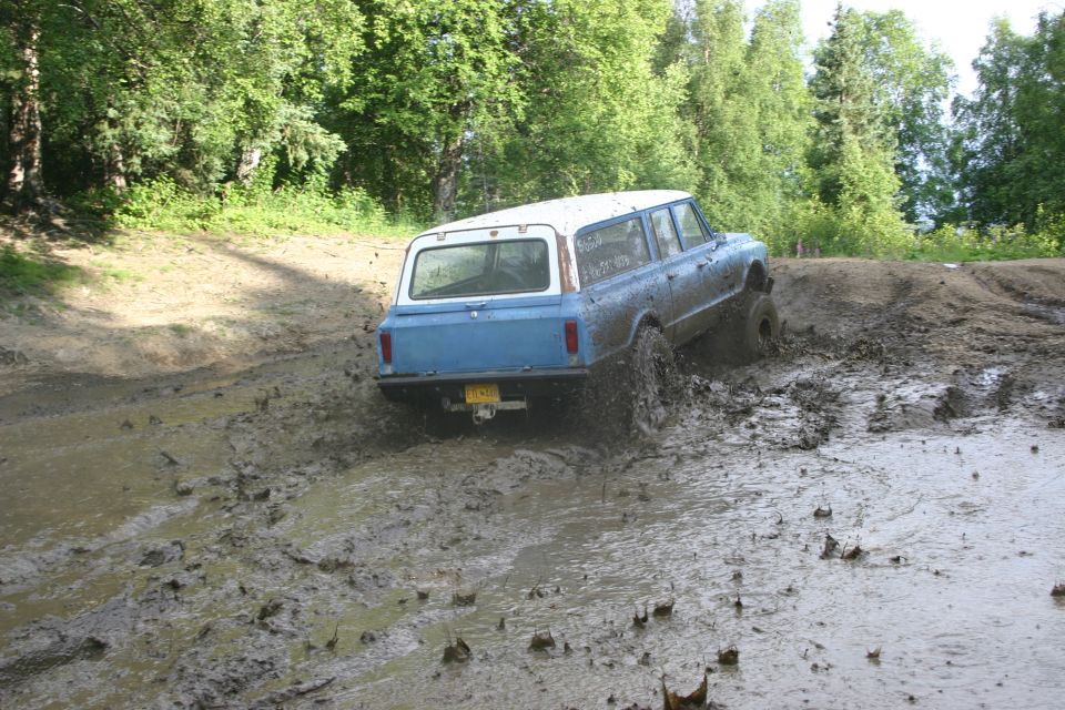 Blue and white long SUV in mud. License plate visible