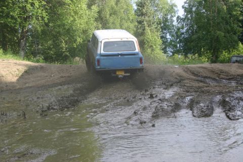 2003 Jeep TJ - SUV navigates a challenging muddy terrain with trees in the background.
