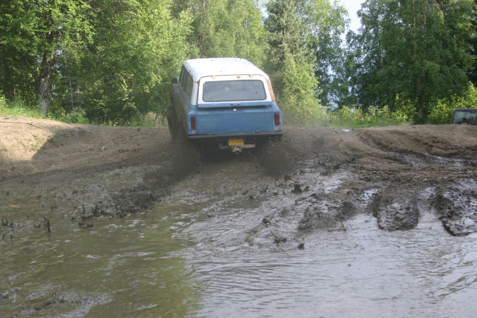 Blue and white SUV with a trailer hitch driving through a muddy puddle on a dirt track