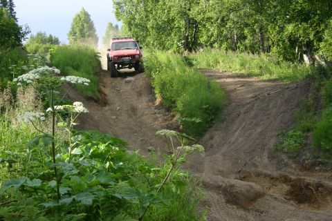 2003 Jeep TJ - A red off-road vehicle navigates a challenging dirt track through a wooded area.