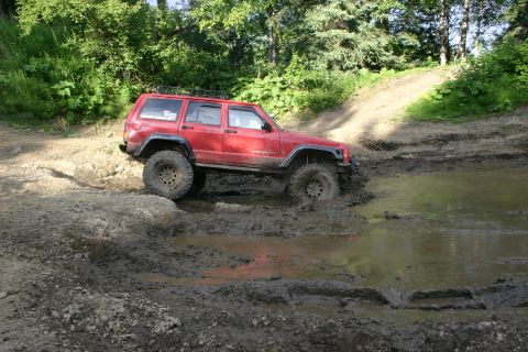 2003 Jeep TJ - A red Jeep Cherokee XJ navigates a muddy trail, demonstrating its off-road capabilities.