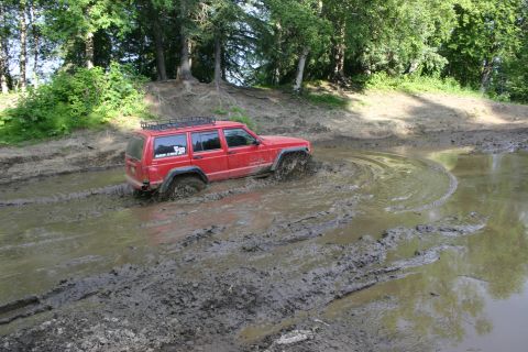 2003 Jeep TJ - A red Jeep Cherokee XJ navigates a muddy trail, its tires deep in the mire.