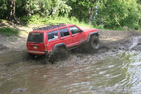 2003 Jeep TJ - A red Jeep Cherokee XJ navigates a muddy trail, splashing water as it goes.