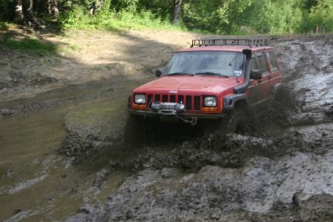 2003 Jeep TJ - A red Jeep Cherokee XJ navigates a muddy trail, equipped with a snorkel and front winch.