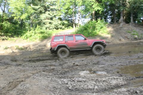 2003 Jeep TJ - Red Jeep Cherokee XJ navigates a challenging muddy off-road course.