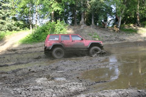2003 Jeep TJ - A red Jeep Cherokee XJ navigates a challenging muddy terrain, kicking up water and mud.