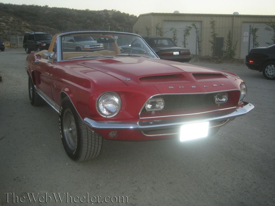 Red Shelby Mustang convertible front view with headlight lit on gravel