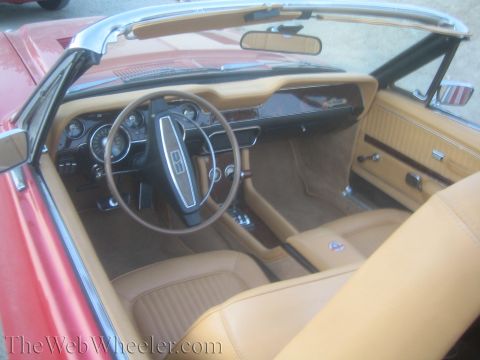 1990 Ford Bronco - Interior view of a red convertible showing a tan dashboard, two-spoke steering wheel and bucket seats with the top down.