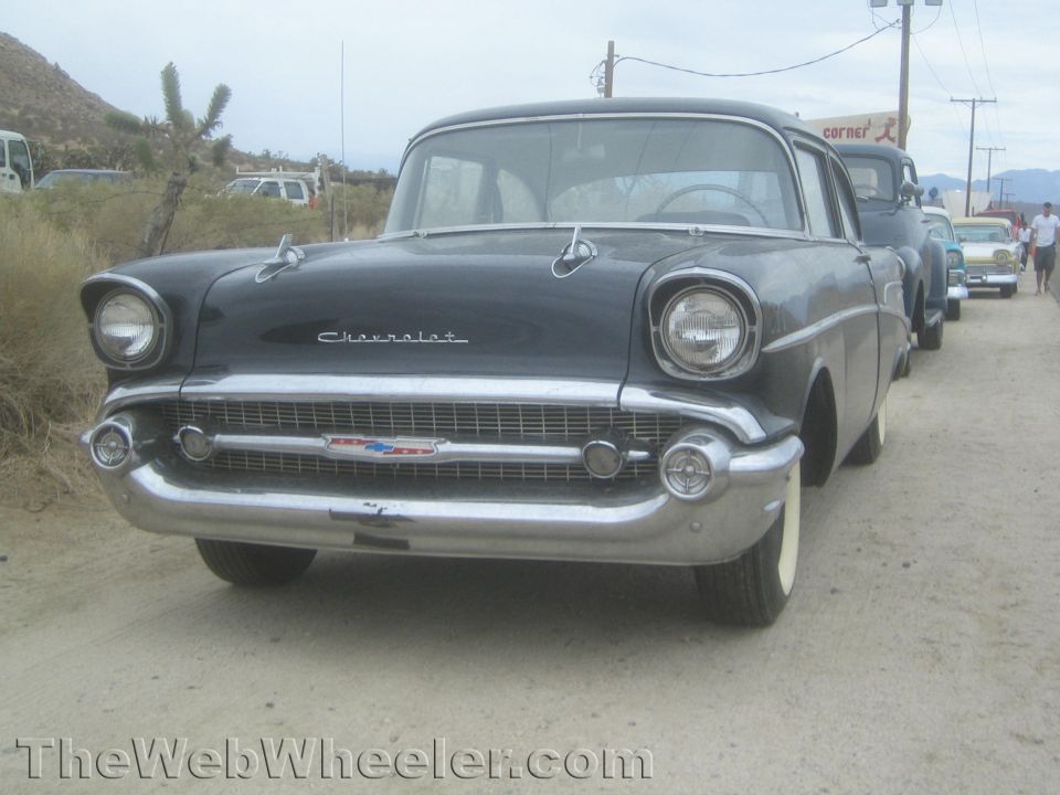 Front of a dark 1957 Chevrolet sedan with chrome grille, desert