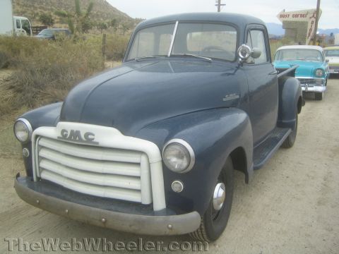 1990 Ford Bronco - dark blue 1950s GMC pickup truck with a white grille and 'GMC' badge parked on a desert roadside.