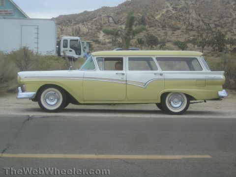 1990 Ford Bronco - Side profile of a two-tone yellow and white 1957 Ford Country Sedan station wagon parked along a desert road.