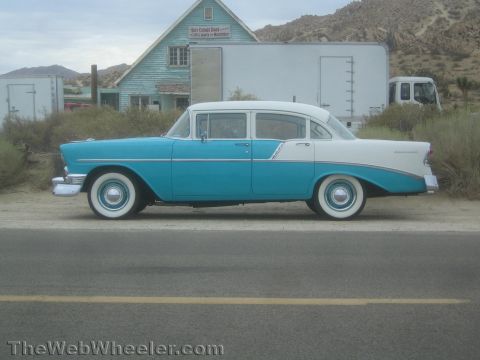 1990 Ford Bronco - Side profile of a turquoise and white 1956 Chevrolet four-door sedan with whitewall tires parked by a rural roadside.