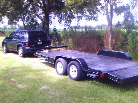 1979 Ford F-150 - A dark-colored SUV is seen from the rear, hitched to a dual-axle flatbed trailer.