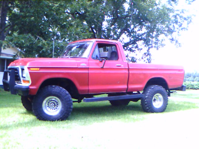 1979 Ford F-150 pickup truck, red, lifted with large tires, parked on grass