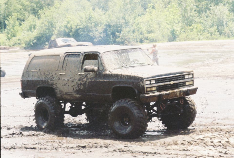 Mud-splattered lifted Chevrolet Suburban on tall mud tires in a mud pit