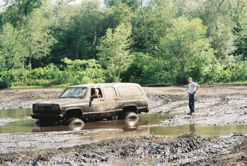 1991 Chevrolet Suburban - A 1991 Chevrolet Suburban is stuck in a muddy water hole, with a person observing from the side.