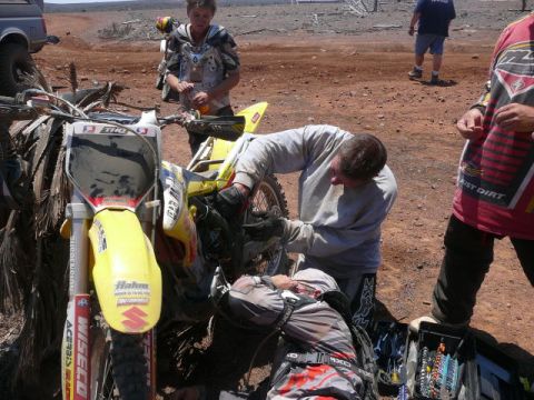 1988 Ford Bronco - Mechanics attend to a dirt bike in a remote, dusty location, with other individuals and vehicles present.