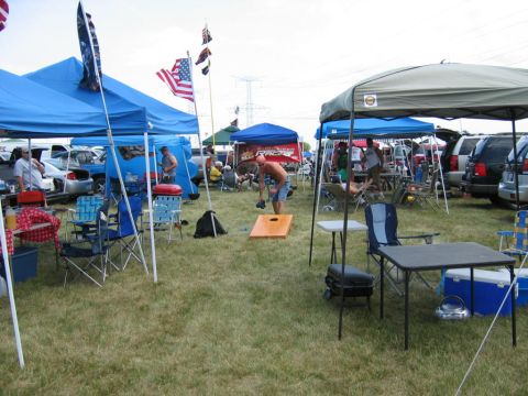 1985 Ford Crown Victoria LTD - A lively tailgate party unfolds with tents, games, and parked vehicles creating a festive atmosphere.