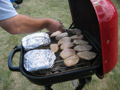 1985 Ford Crown Victoria LTD - Chicken and foil-wrapped food are grilled on a red portable grill.