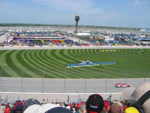 1985 Ford Crown Victoria LTD - View of Chicagoland Speedway during a NASCAR event, showing the track, grandstands, and a full parking area.