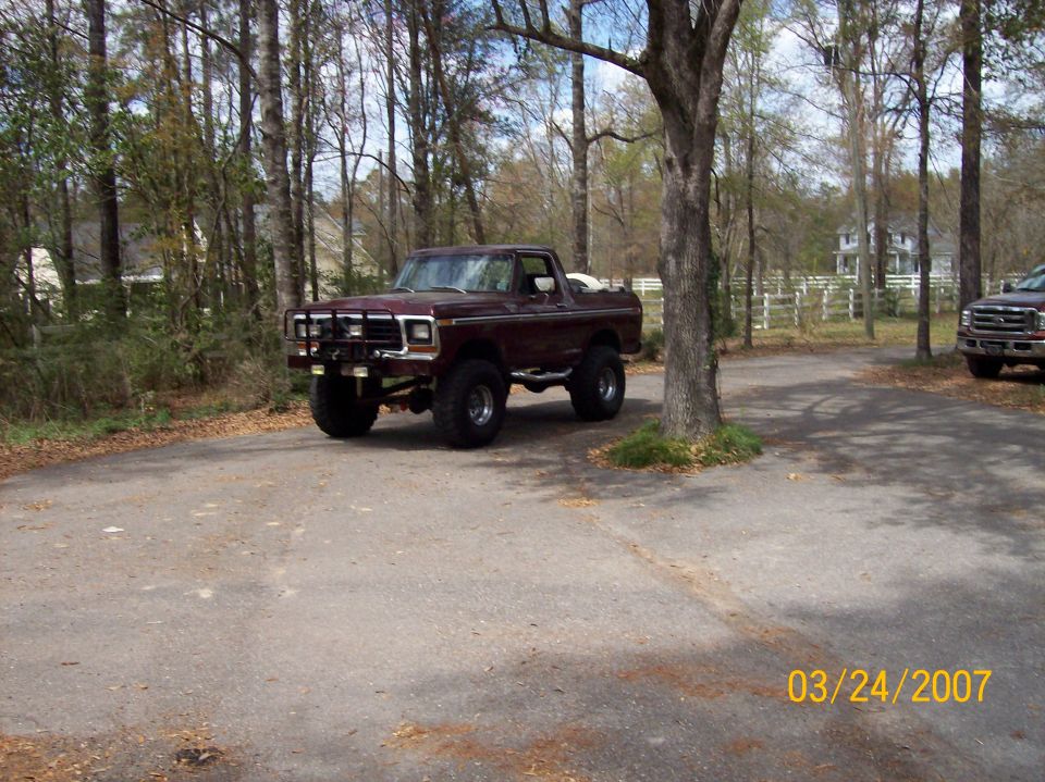 Maroon lifted Ford Bronco with brush guard parked on driveway among trees