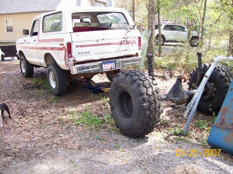 1978 Ford Bronco - White 1978 Ford Bronco with red stripe accents sits on a gravel lot, with a large spare tire and axle in the foreground.