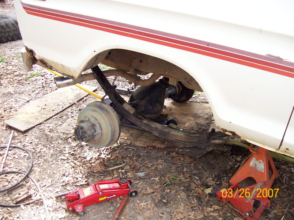White truck with rear wheel off showing leaf spring, axle housing and disc brake rotor