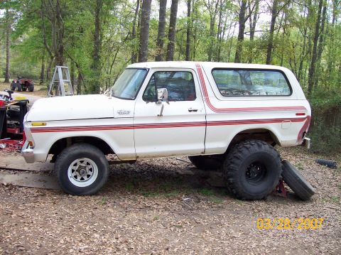 1978 Ford Bronco - A lifted 1978 Ford Bronco with custom wheels and tires sits on jacks in a wooded area.