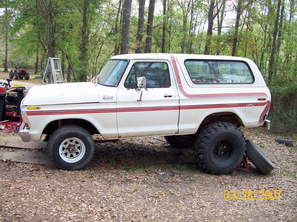 White 1978 Ford Bronco with red stripe accents, lifted with large tires, parked outdoors