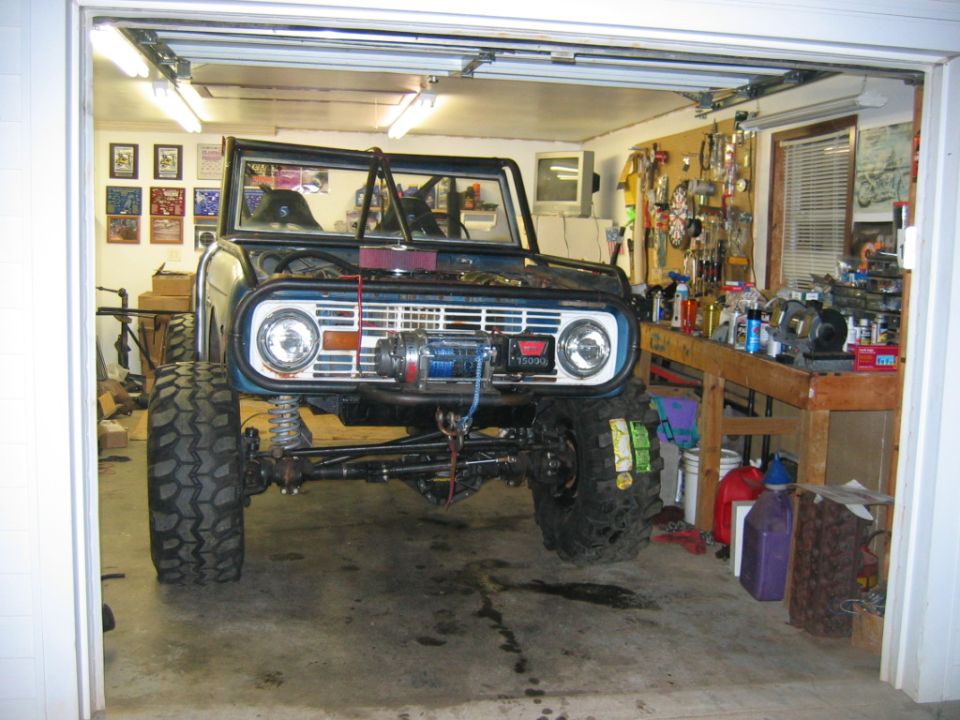 Blue 1974 Ford Bronco with winch, off-road tires, and roll cage, parked in a garage