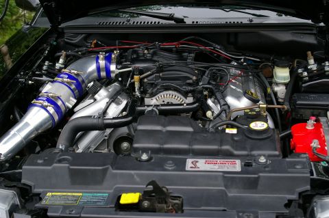 1995 Ford Probe - Open engine bay of a supercharged Ford Mustang Cobra showing a polished aluminum cold-air intake tube joined by blue silicone couplers and…