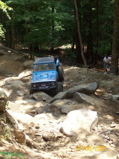 1978 Ford Bronco - A blue off-road vehicle tackles a challenging rocky path in a wooded area.