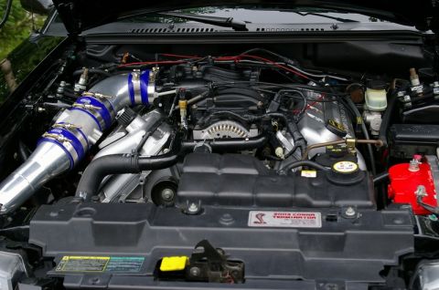 1995 Ford Probe - Engine bay of a supercharged Ford Mustang Cobra with the hood raised, showing a polished mandrel-bent intake pipe with blue silicone couple…