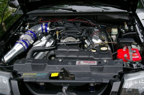1995 Ford Probe - Wide view into the engine bay of a black supercharged Ford Mustang Cobra, hood open, showing the polished intake pipe with blue silicone co…