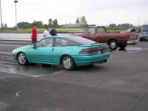1996 Ford Probe - A teal 1996 Ford Probe is parked on asphalt next to a brown Dodge Ram pickup truck and other vehicles.