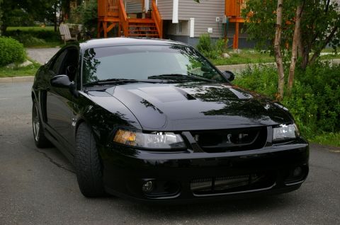 1995 Ford Probe - Glossy black New Edge Ford Mustang coupe parked on an asphalt driveway, shot from the passenger-side front three-quarter angle. The cowl ho…