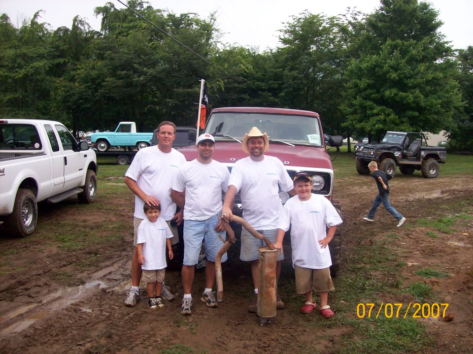 Group of men and boys in white shirts posing in front of trucks at an outdoor event