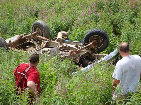 2000 Ford E350 - An overturned vehicle lies on its side in a grassy field, with two men observing the scene.