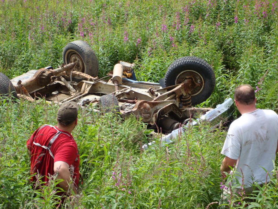 Two guys looking at an overturned vehicle chassis in a field of tall grass and flowers