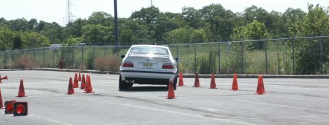 2001 Mercury Grand Marquis - A white BMW sedan is seen from the rear, driving through an obstacle course marked by traffic cones.