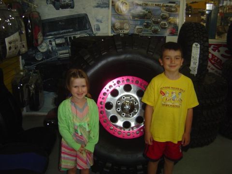 1986 Ford F-150 - Children pose in front of a massive tire and custom wheel, likely at a tire shop or auto show.