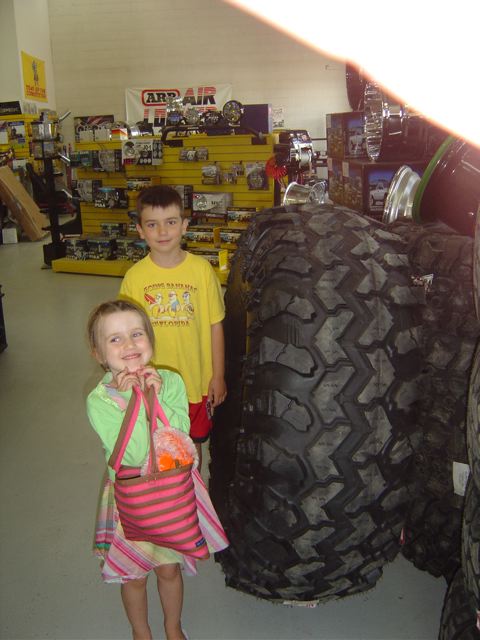 1986 Ford F-150 - Two children stand in an auto parts store, dwarfed by a display of massive tires.