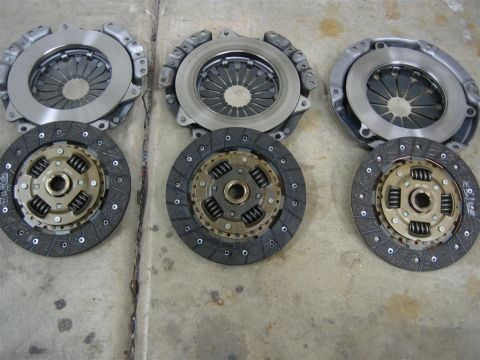 1987 Suzuki Samurai - Three automotive clutch kits are displayed on a concrete surface, ready for installation or comparison.